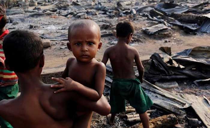 Seorang anak menggendong adiknya diantara reruntuhan puing desa yang dibakar tentara Myanmar, di Provinsi Rakhine, hari Senin lalu. (foto: afp)