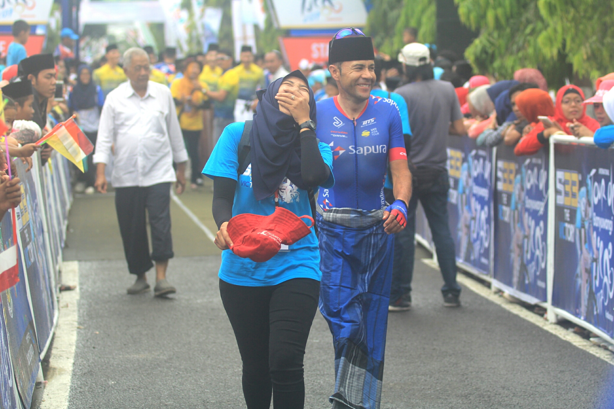 Petugas  LO Internasional Tour de Banyuwangi Ijen 2017 terbahak melihat para pebalap asing bingung cara  sarungan. foto:ngopibareng.id/tom 