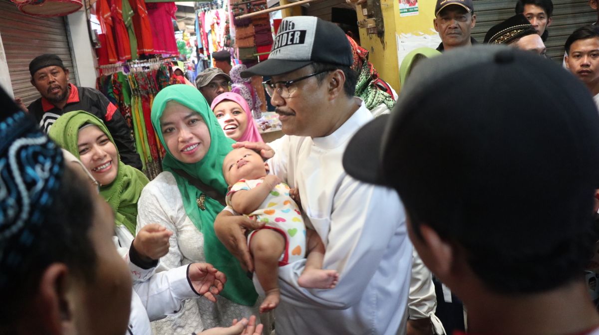 Gus Ipul membantu seorang ibu dengan anak bayinya yang kesulitan menembus kerumunan pembeli di pasar, 