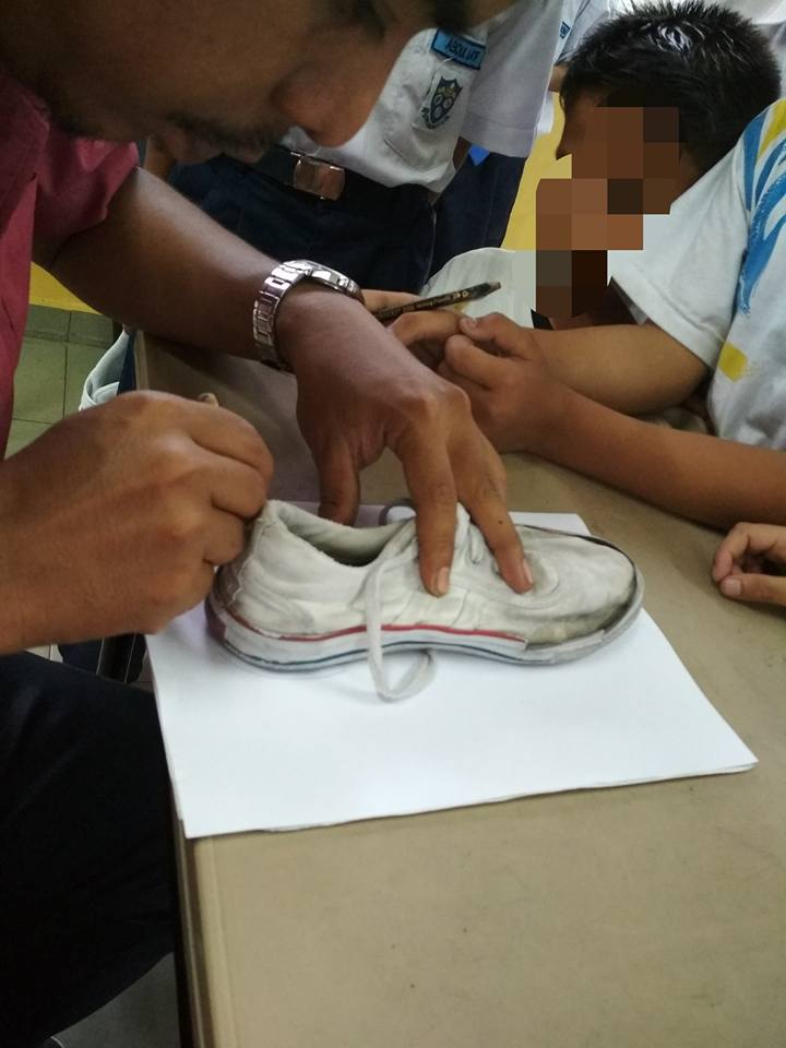 Mohd. Fadli Salleh menggambar sepatu usang murid-muridnya untuk mengetahui ukurannya.