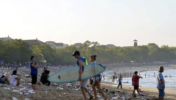 Dokumentasi wisatawan membawa papan selancar berjalan di antara ceceran sampah perayaan Tahun Baru 2016 di Pantai Kuta, Bali, Jumat 1 Januari. Kebiasaan tercela membuang sampah sembarangan pada perayaan pergantian tahun di kawasan wisata tersebut berulang setiap tahun sehingga sangat mengganggu kenyamanan wisatawan. (Foto: Antara)