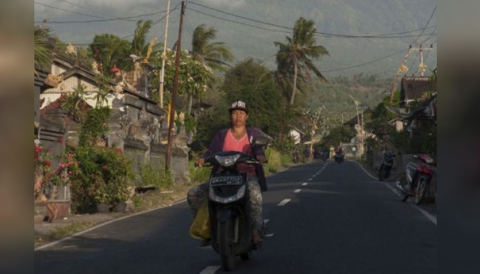 Warga mengendarai sepeda motor dengan latar belakang erupsi Gunung Agung di Desa Culik, Karangasem, Bali, Jumat 29 Juni 2018. (Foto: Antara)