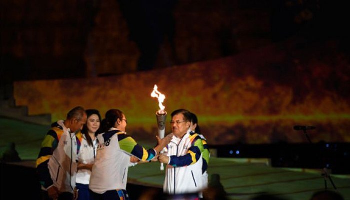 Wapres Jusuf Kalla (kanan) disaksikan legenda bulu tangkis Indonesia Susi Susanti (kedua kiri) dan mantan atlet tenis Yustedjo Tarik (kiri) menyerahkan api obor Asian Games 2018 yang telah disatukan kepada mantan atlet bulu tangkis Finarsih (kedua kanan) saat Asian Games 2018 Torch Relay Concert di Kompleks Candi Prambanan, Sleman, DI Yogyakarta, Rabu 18 Juli 2018. Penyatuan api obor dari India dan Mrapen tersebut menandai dimulainya perjalanan api obor Asian Games 2018 yang akan dibawa berlari mengelilingi 18 provinsi. (Foto: Antara)