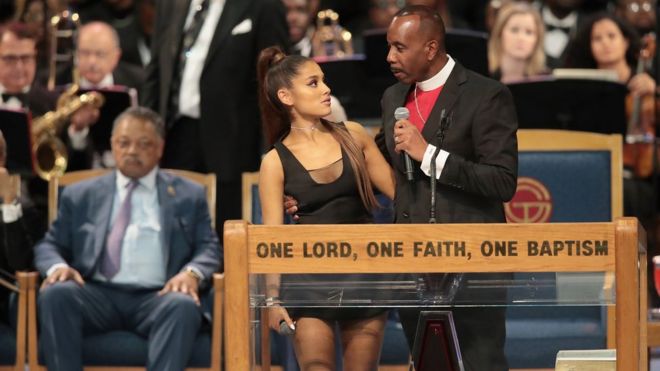 Posisi tangan Bishop Charles H Ellis III tidak wajar. Ia bukan memeluk pinggang Ariana Grande, tetapi (maaf) di bagian dada. Foto: GETTY IMAGE.