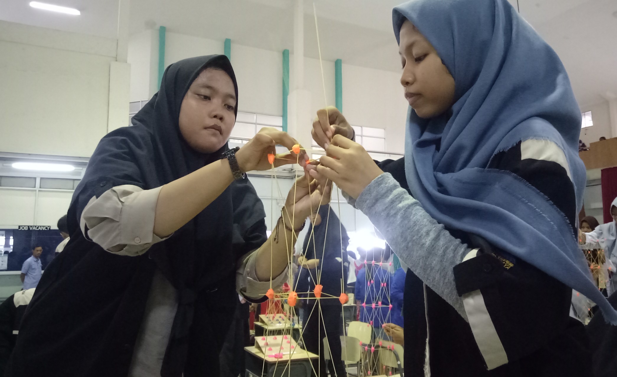 Dinda Bayu (kiri)  dan Aura Dian (kanan)  sedang berkonsentrasi untuk menyusun menara dari pasta. (foto:pita/ngopibareng.id)