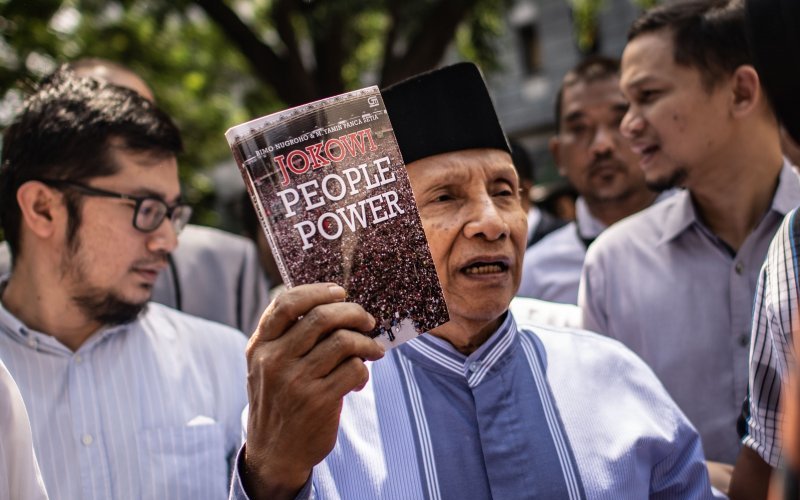 Ketua Dewan Kehormatan Partai Amanat Nasional (PAN) Amien Rais (tengah) menunjukkan buku berjudul Jokowi People Power saat jeda pemeriksaan untuk Shalat Jumat di Direktorat Reserse Kriminal Umum (Ditreskrimum) Polda Metro Jaya, Jakarta, Jumat 24 Mei 2019. Amien Rais diperiksa sebagai saksi atas kasus dugaan makar dengan tersangka Eggi Sudjana. (Foto: Antara/Aprillio Akba)