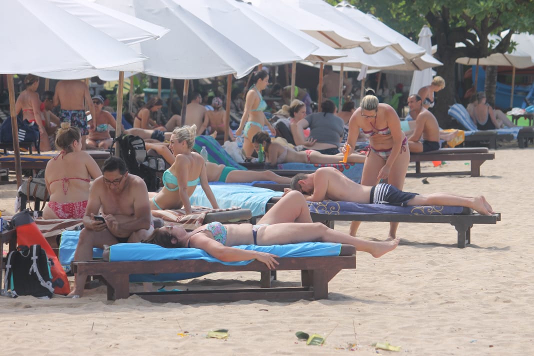 Wisman saat santai dan berjemur di Nusa Dua Beach. Anak anak pun asyik bermain di pasir putih, dan seoranf widatawan domestik menyuri pantai Nusa Dua. (Foto: Asmanu/ngopibareng.id)