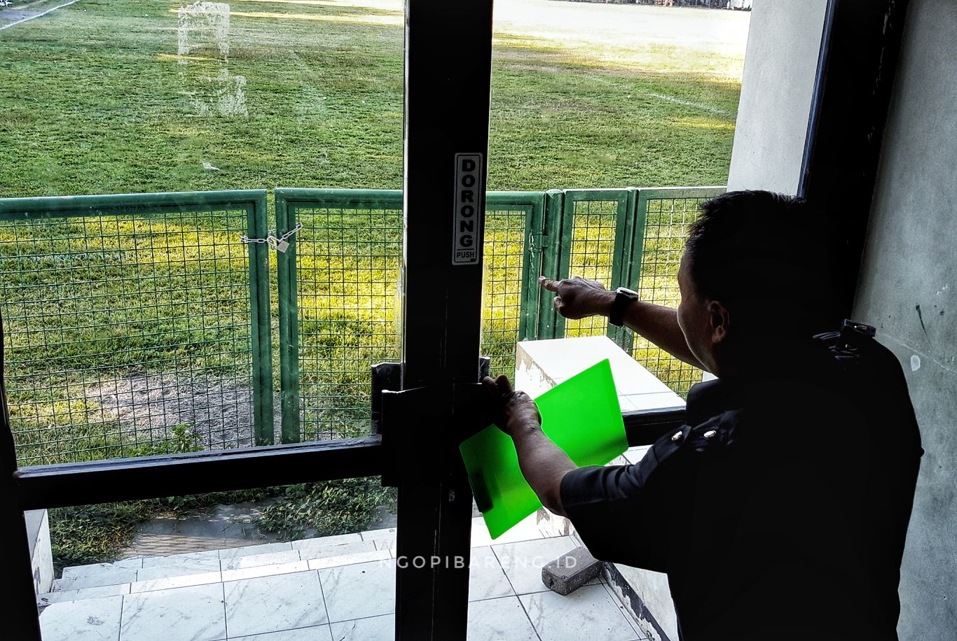 Pengawas Pertandingan menyaksikan pagar Lapangan Karanggayam yang digembok. (Foto: Haris/ngopibareng.id)