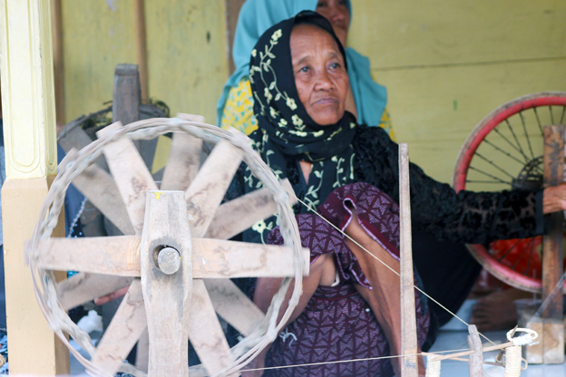 Sudah sepuh, bekerja dalam kerentaan. Tapi keahliannya memintal benang dari kapas dengan alat sederhana bukan main ahlinya. (Foto:WidiKamidi/ngopibareng.id) 