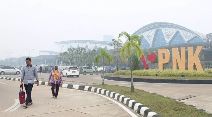 Warga berjalan di kompleks Bandara Supadio yang diselimuti kabut asap di Kabupaten Kubu Raya, Kalimantan Barat, Minggu 15 September 2019. Maskapai Garuda Indonesia membatalkan setidaknya tiga rute penerbangan Jakarta-Pontianak pada Minggu 15 September 2019. (Foto: Antara/Jessica Helena Wuysang)