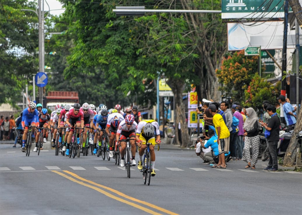 Pembalap saat melintas di Kecamatan Genteng, Kabupaten Banyuwangi. Etape pertama International Tour de Banyuwangi Ijen (ITdBI) 2019 menjadi milik pembalap asal Mongolia, Maral-Erdene Batmunkh dari Terengganu Inc. TSG Cycling Team (Malaysia). Batmunkh melahap rute sejauh 133,2 kilometer dengan catatan waktu 3 jam, 3 menit dan 36 detik.  disusul oleh Robbie Hucker dari Ukyo Team di posisi kedua dan  Jesse Ewart dari Sapura Cycling Team di posisi ke tiga. (Foto: Japrak/ngopibareng.id)