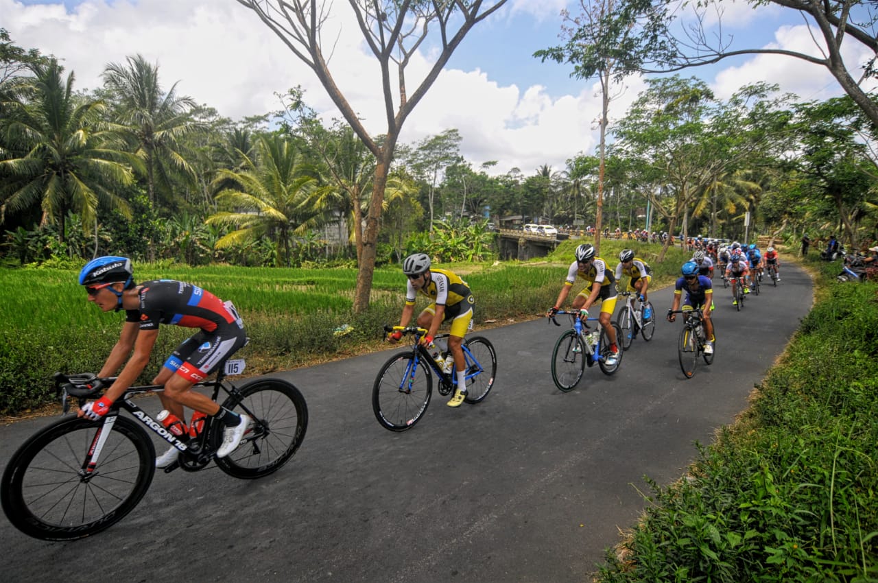 Pebalap saat melintas di area persawahan Kecamatan Songgon, Kabupaten Banyuwangi. Etape pertama International Tour de Banyuwangi Ijen (ITdBI) 2019 menjadi milik pembalap asal Mongolia, Maral-Erdene Batmunkh dari Terengganu Inc. TSG Cycling Team (Malaysia). Batmunkh melahap rute sejauh 133,2 kilometer dengan catatan waktu 3 jam, 3 menit dan 36 detik.  disusul oleh Robbie Hucker dari Ukyo Team di posisi kedua dan  Jesse Ewart dari Sapura Cycling Team di posisi ke tiga. (Foto: Japrak/ngopibareng.id)