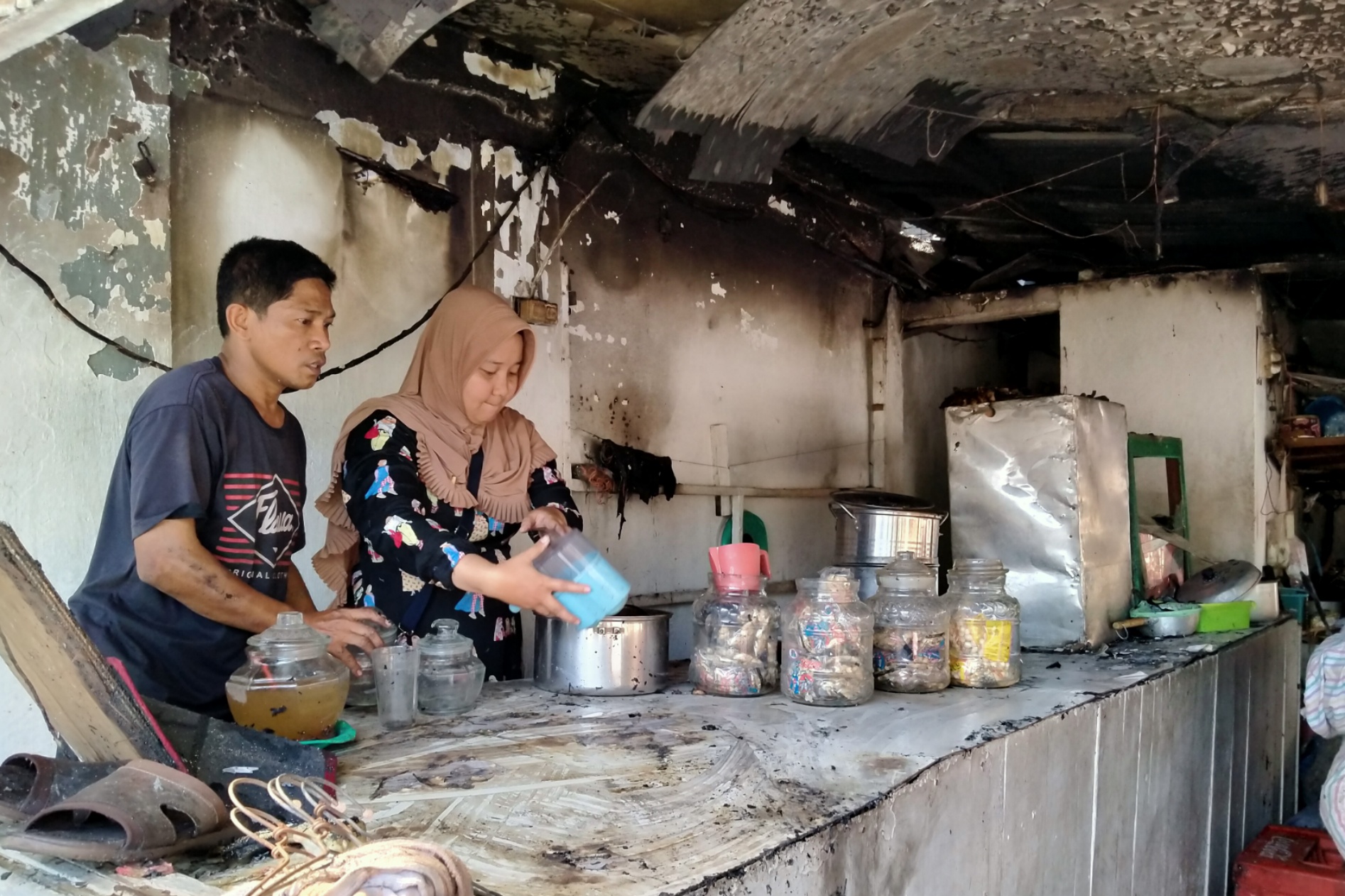 Pedagang es degan, Yuyun (kanan) dibantu warga membersihkan tempat dagangnya yang terbakar, Sabtu 16 November 2019. (Foto: Fariz/ngopibareng.id)