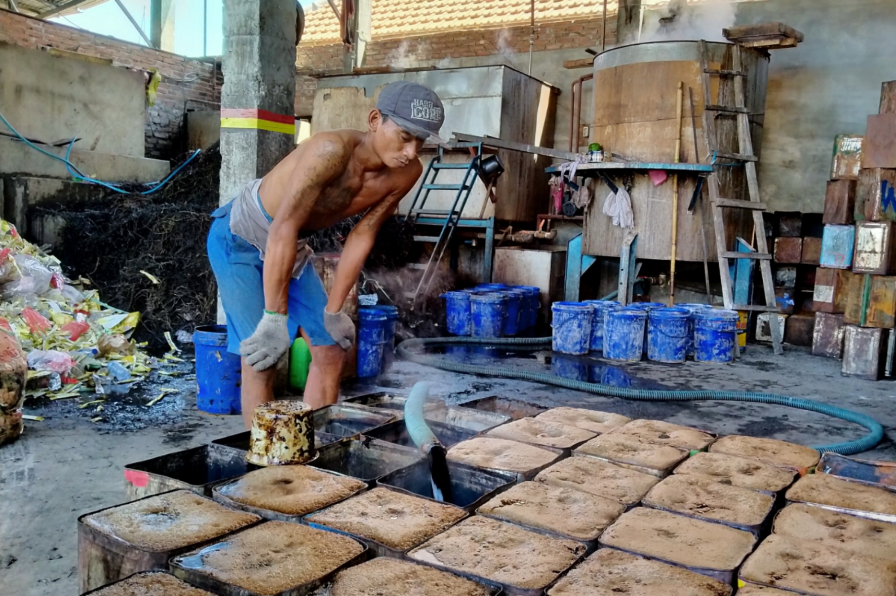 Salah satu pekerja industri cao memindahkan cairan dari panci masak ke dalam kaleng bekas minyak goreng. (Foto: Fariz/ngopibareng.id)