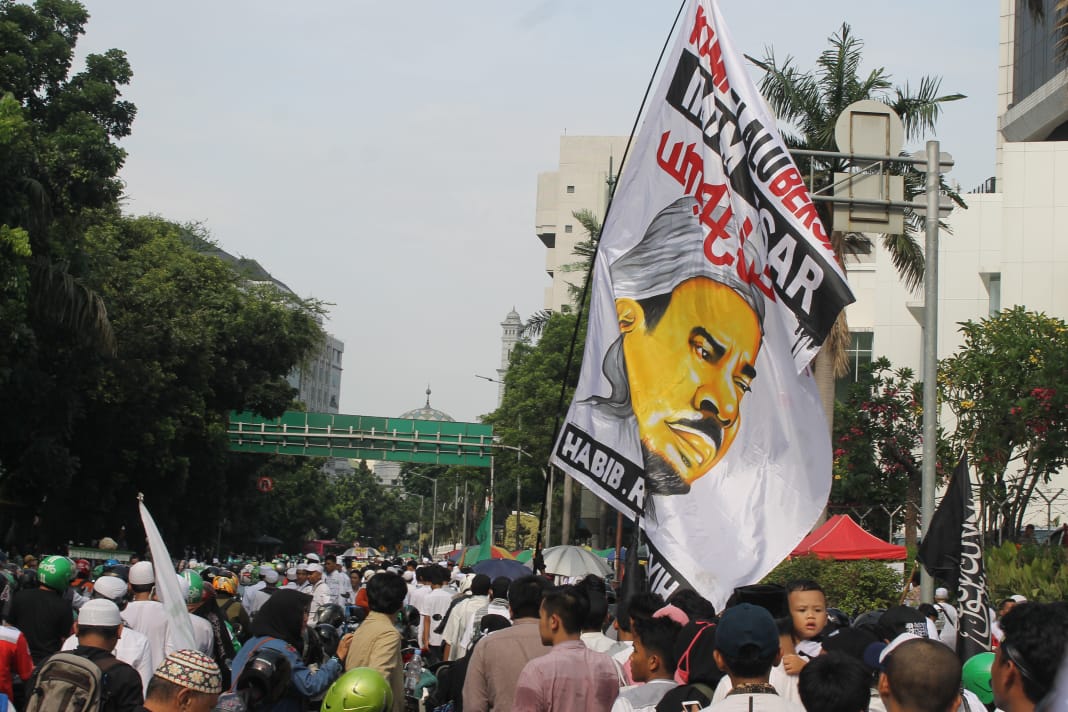 Massa peserta Reuni PA 212 mengibarkan bendera bergambar M Rizieq Syihab. Mereka minta supaya pemimpin mereka dipulangkan ke Indonesia. (Foto: asmanu/ngopibareng.id)