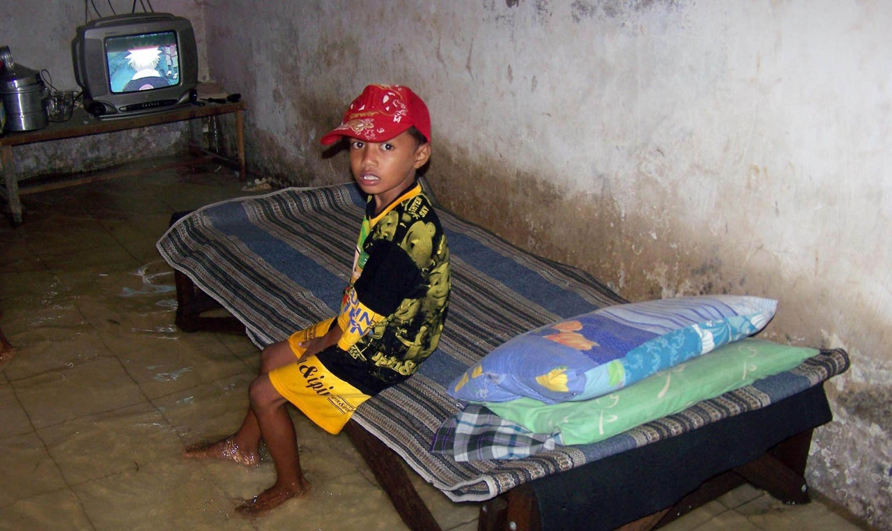 Seorang bocah di Kampung Dok, Kota Probolinggo nonton TV di saat banjir menggenangi rumahnya. (Foto: Ikhsan/ngopibareng.id)