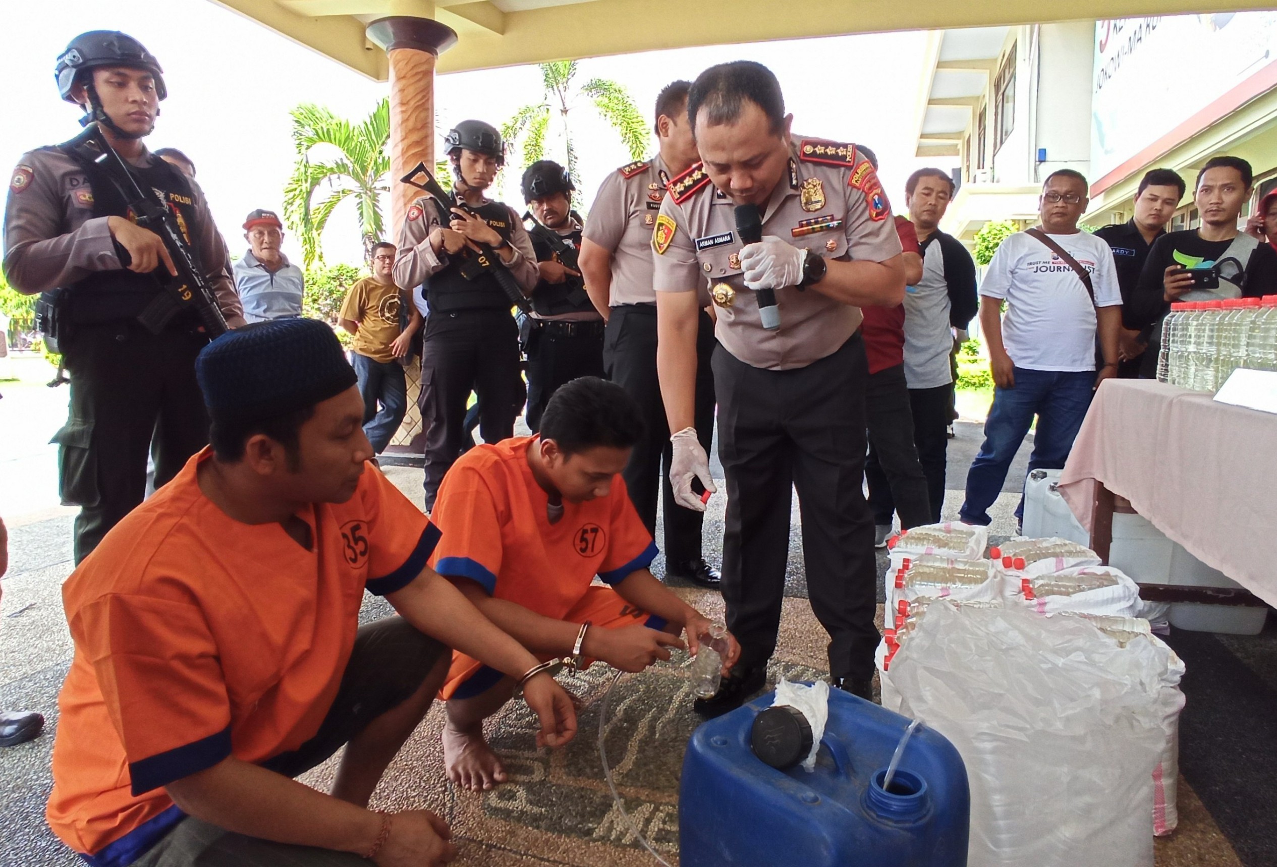 Kapolresta Banyuwangi Kombespol Arman Asmara Syarifudin memperhatikan pelaku uang memperagakan cara pengoplosan minuman keras berbahan etanol (foto : Hujaini/ngopibareng.id)