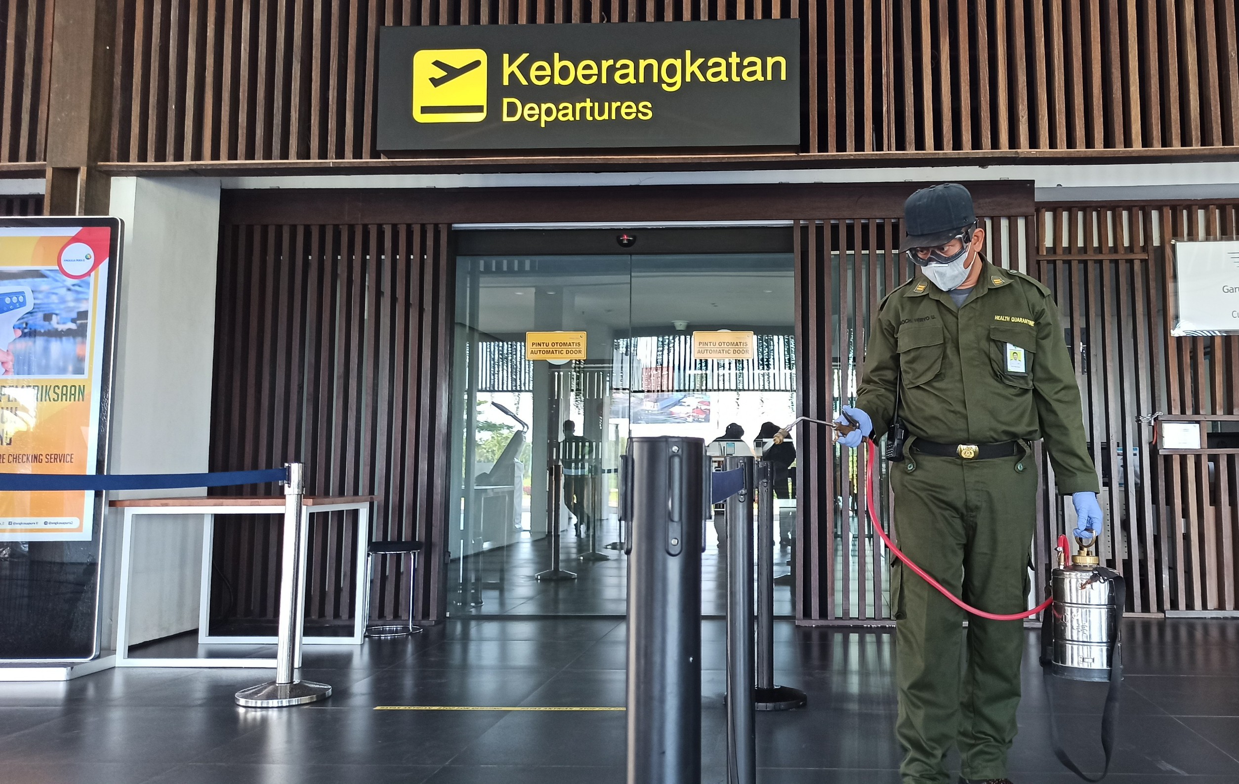 Petugas sedang menyemprotkan cairan disinfektan di pintu masuk ruang keberangkatan Bandara Blimbingsari, Banyuwangi, Jawa Timur. (Foto: Muh Hujaini/Ngopibareng.id)