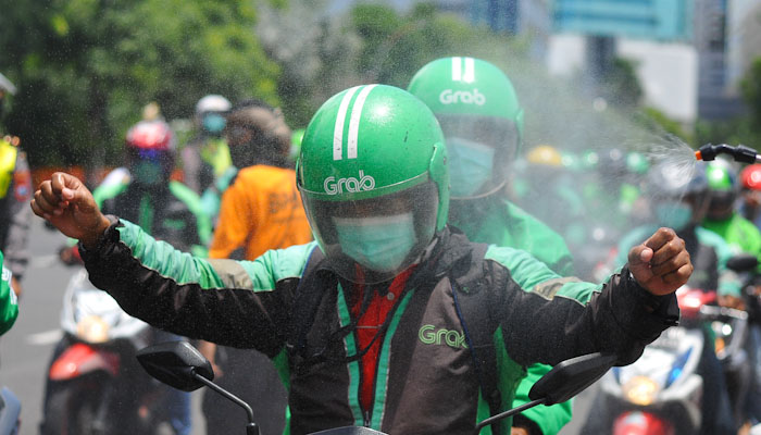 Driver ojol disemprot disinfektan saat melintas di depan gedung Grahadi Surabaya. (foto : Erfan Hazransyah/Ngopibareng.id)