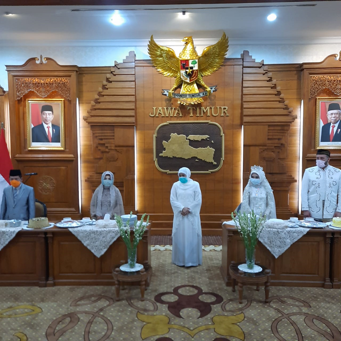 Sembari menggunakan masker, Gubernur Jawa Timur Khofifah Indar Parawansa berdiri di antara dua pasangan pengantin yang resepi di Grahadi. (Foto: Alief Sambogo/Ngopibareng.id)