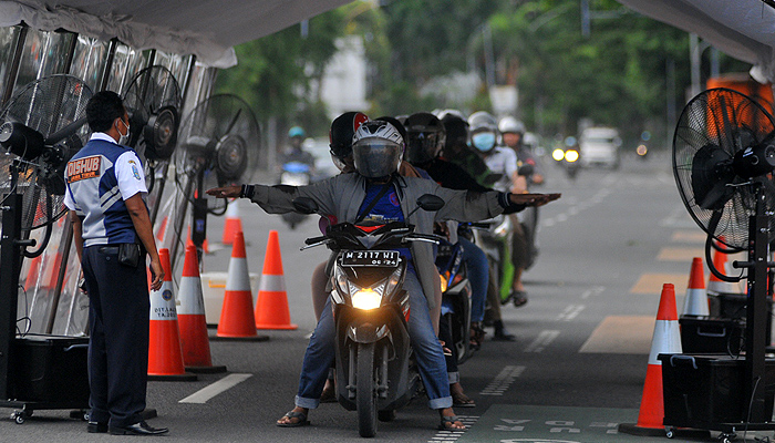 Petugas Dinas Perhubungan (Dishub) Jawa Timur memberi aba-aba agar kendaraan yang melintas di dalam bilik penyemprotan disinfektan untuk menghentikan kendaraannya sebentar. (Foto: Erfan Hazransyah/Ngopibareng.id)