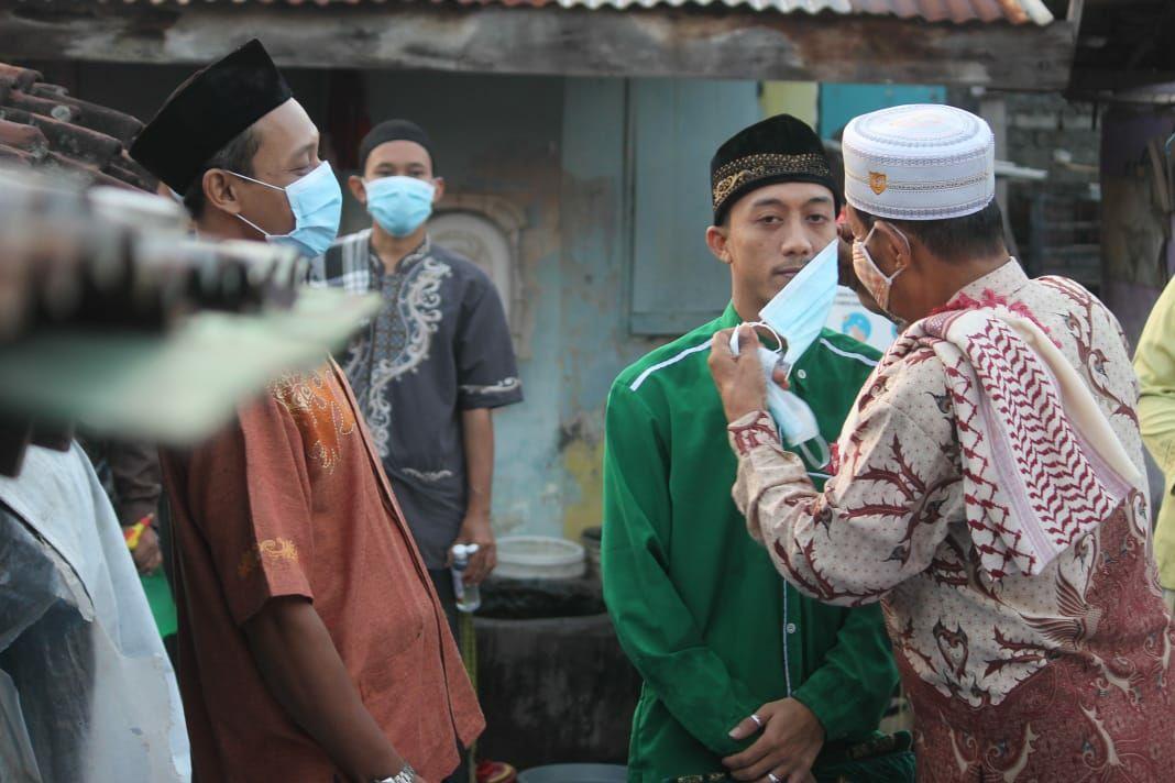 Warga membantu memasangkan masker pada jemaah yang lalai tak menggunakan masker. (Asmanu Sudharso/Ngopibareng.id)