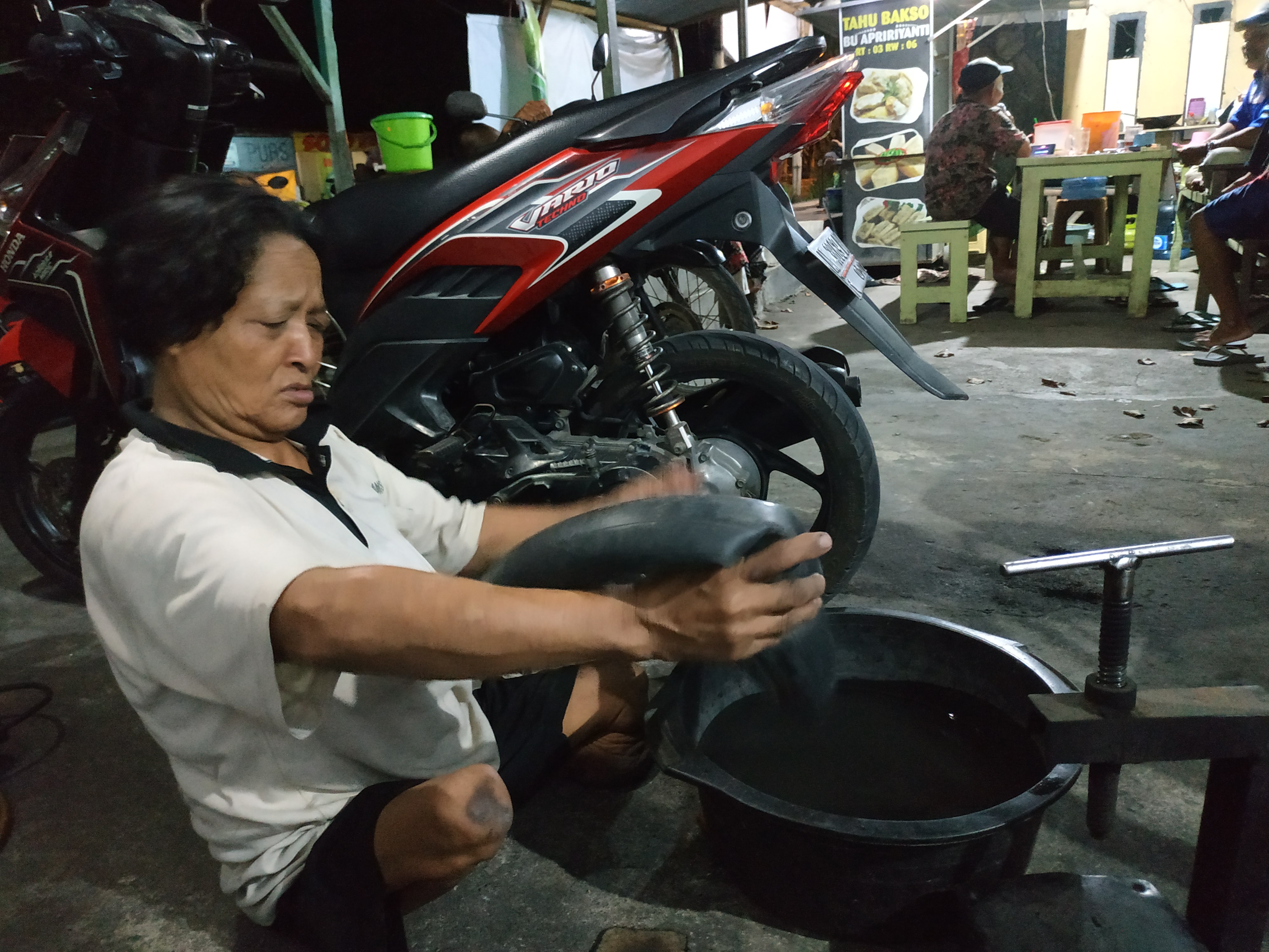 Kasiani, perempuan disabilitas ini  sedang menambal ban untuk kebutuhan hidup. (Foto: Fendhy/Ngopibareng.id)