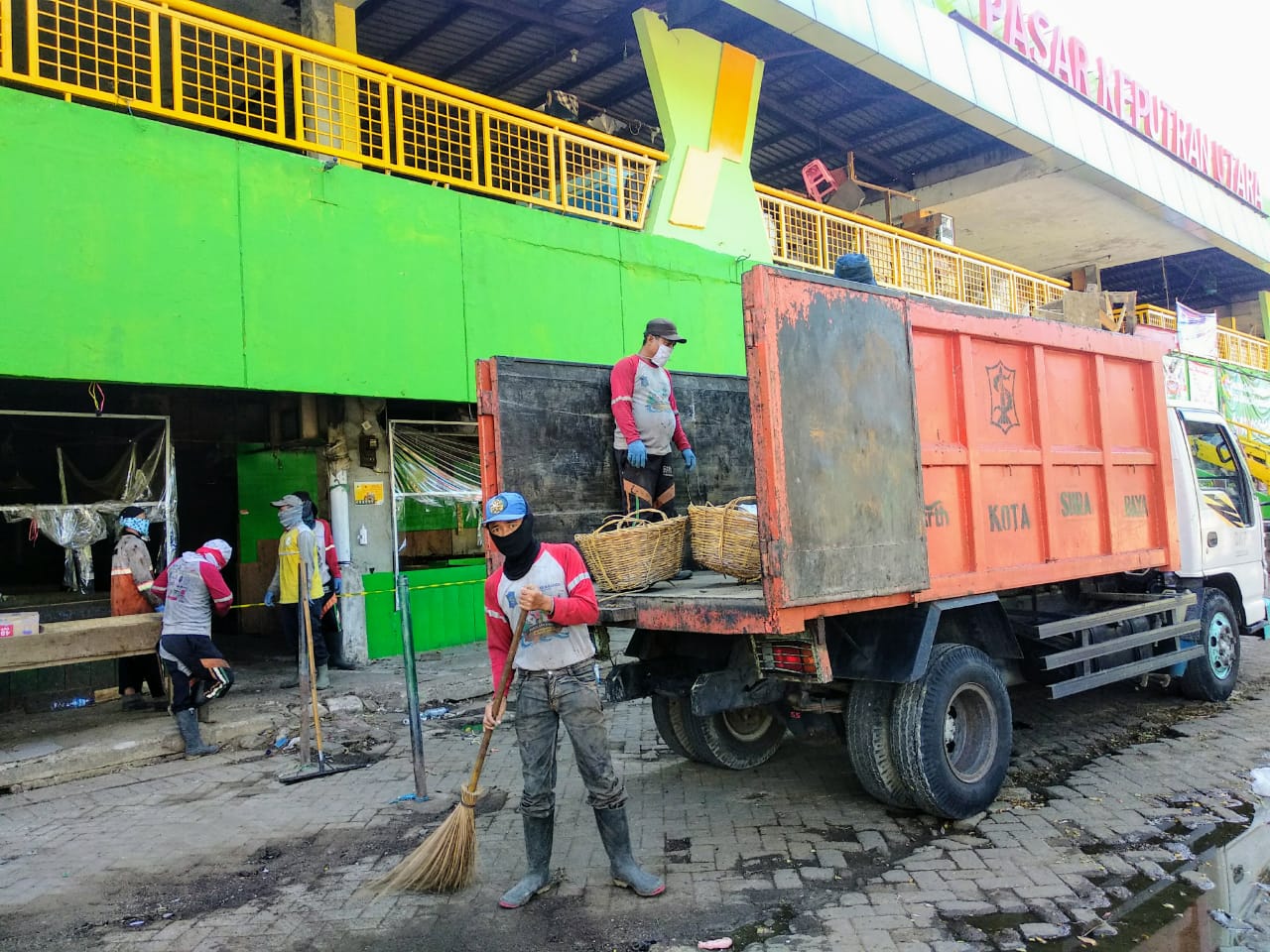 Sejumlah petugas Dinas Kebersihan dan Ruang Terbuka Hijau (DKRTH) Surabaya tampak membersihkan halaman depan Pasar Keputran dengan memakai masker. Sebagian yang lain mengangkut hasil sampah ke dalam truk. (Foto: M.Rizqi/Ngopibareng.id)