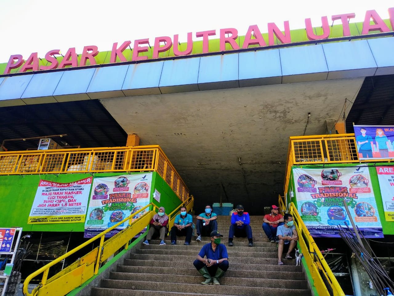 Sejumlah petugas PD Pasar Surya dengan mengenakan masker. Mereka beristirahat di tangga menuju pintu masuk pasar setelah melakukan kerja bakti membersihkan area pasar dari depan hingga belakang. (Foto: M.Rizqi/Ngopibareng.id)