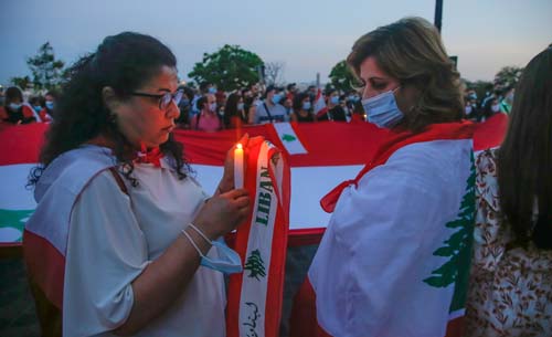 Beberapara orang menyalakan dan memegang lilin untuk mengenang para korban ledakan mematikan di Beirut di depan Basilika Sacre Coeur di Paris, Prancis. (Michel Euler/AP)