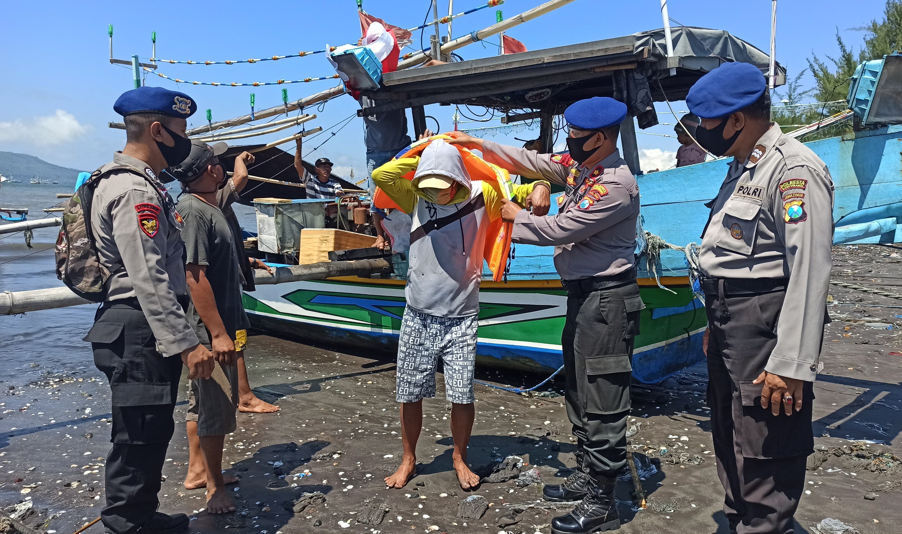 Kasatpolairud Polresta Banyuwangi memakaikan life jacket pada salah satu nelayan. (Foto: Muh Hujaini/Ngopibareng.id)