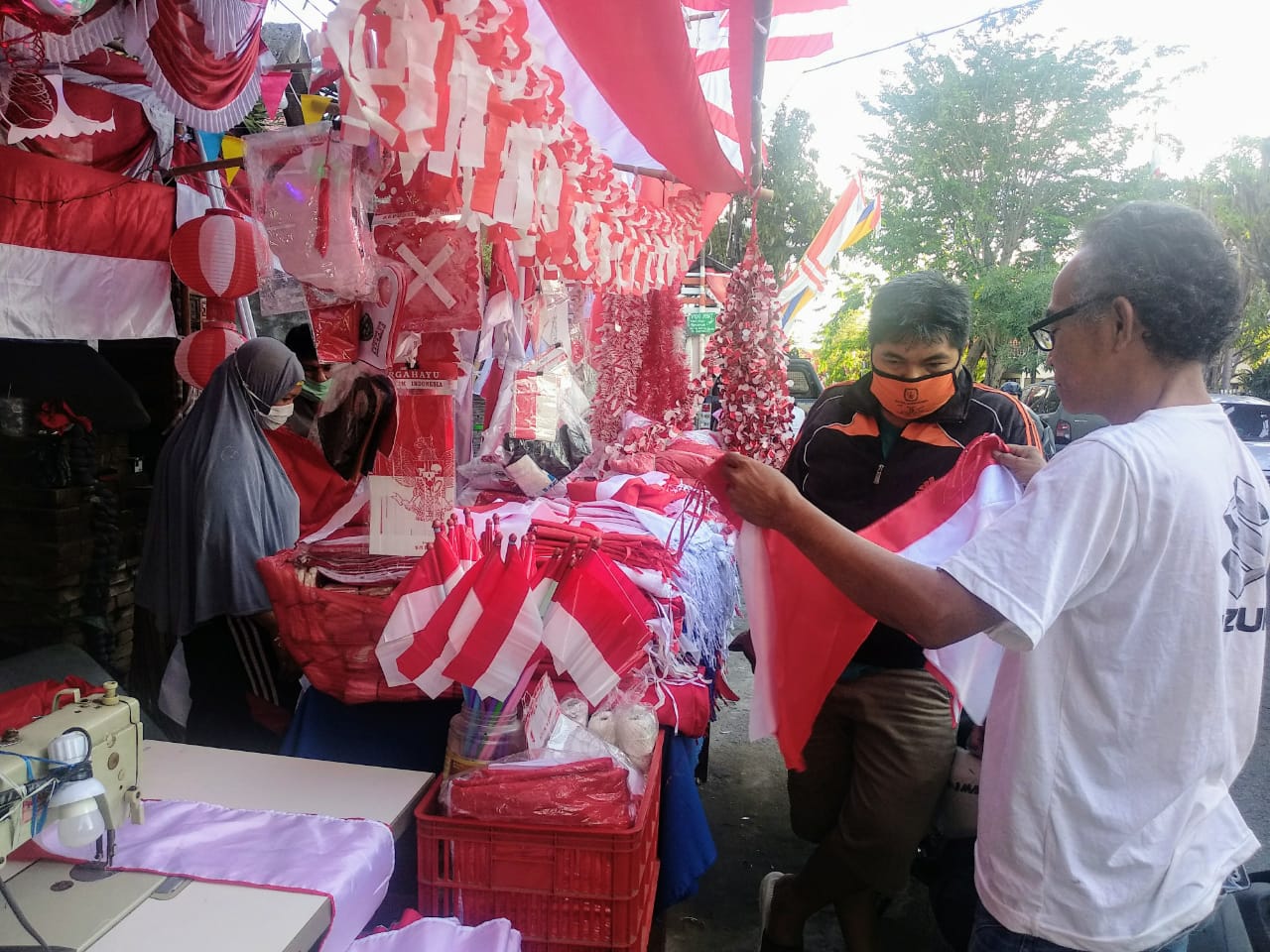 Salah satu pedagang menunjukkan contoh bendera ke seorang pembeli. Pedagang itu memakai kacamata dan berbaju putih (Foto: M.Rizqi/Ngopibareng.id)