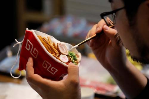 Seniman Jepang Takahiro Shibata sedang menyelesaikan masker bergambar semangkuk ramen atau mie kuah ala Jepang. (Foto:Reuters)