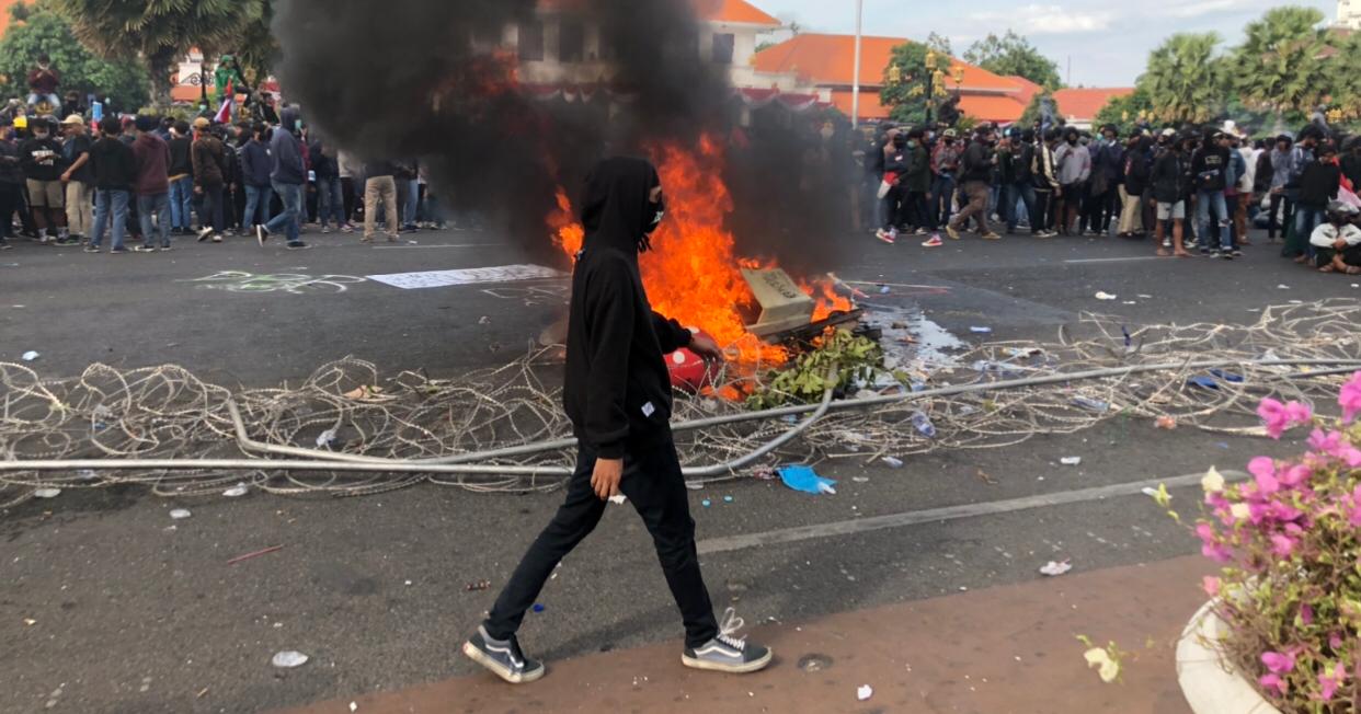 Foto salah seorang demonstran berjalan di depan kobaran api di sela-sela aksi. (Foto: Andhi Dwi/Ngopibareng.id)