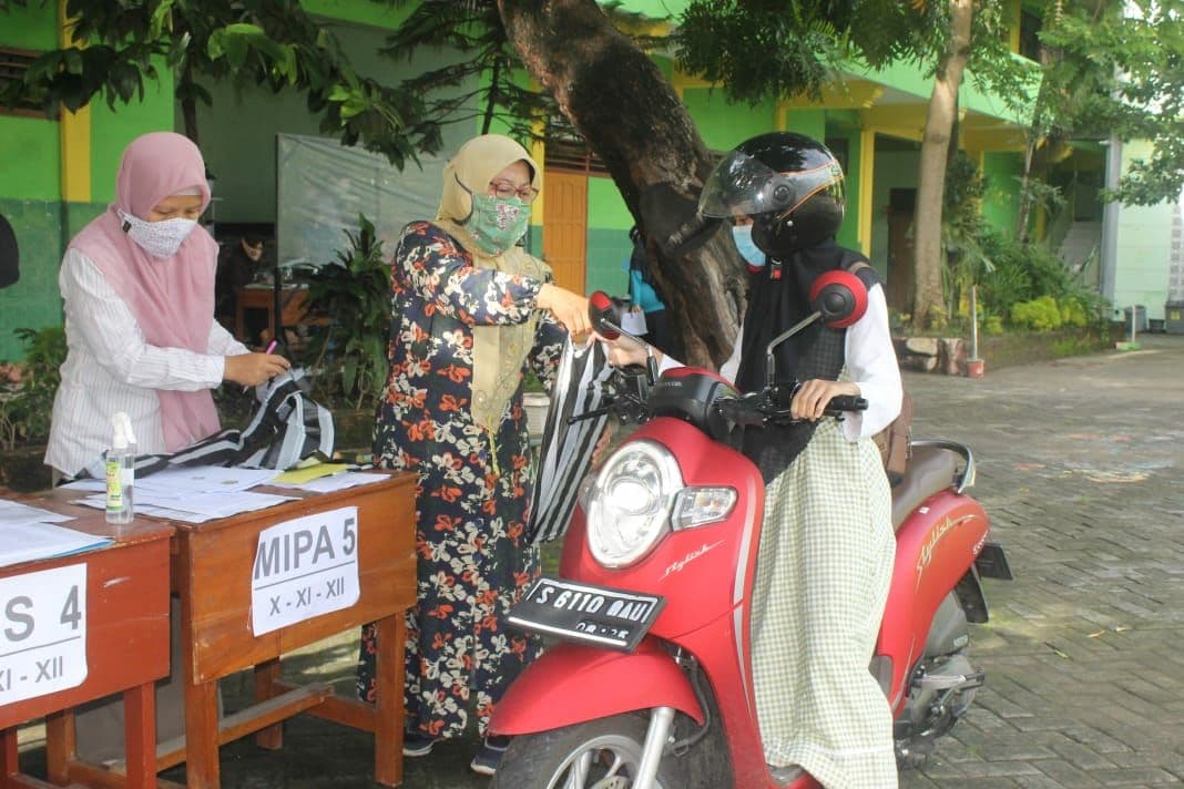 Kepala MAN I Jombang Erma Rahmawati, saar membagikan rapot tahun ajaran ganjil kepada anak didiknya dengan sistem drive thru. ( foto: asmanu/ngopibareng.id)