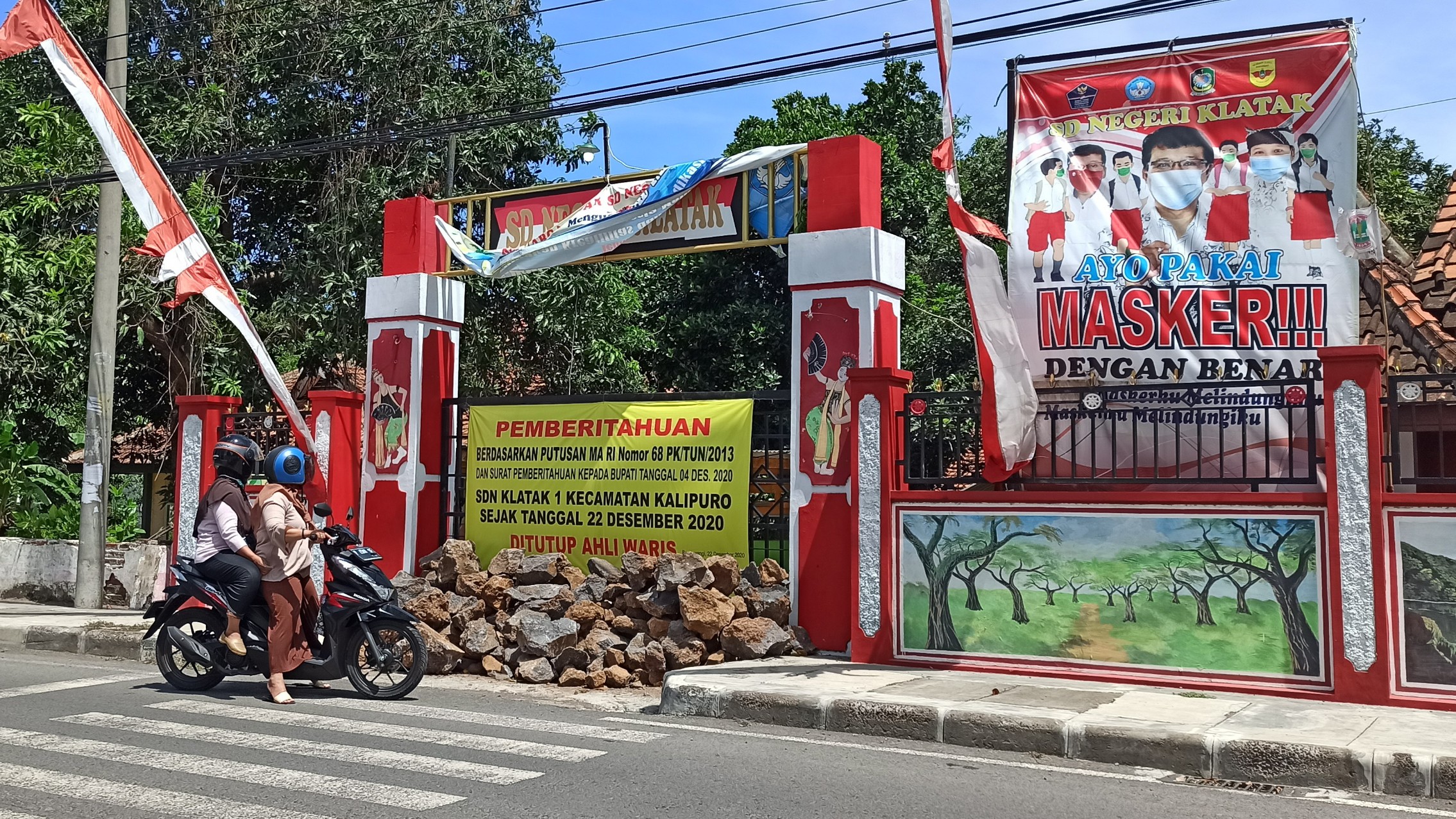 Seorang warga sedang membaca banner penutupan SDN 1 Klatak, Kecamatan Kalipuro, Banyuwangi. (Foto: Muh Hujaini/Ngopibareng.id)