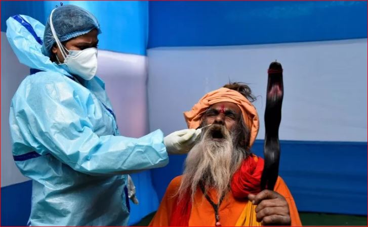 Seorang Sadhu atau seorang pria suci Hindu bereaksi saat tenaga kesehatan memakai Alat Pelindung Diri (APD) mengambil sampe usab darinya untuk tes rapid antigen di sebuah tempat penampungan dimana para peziarah berkumpul sebelum melakukan perjalanan tahunan menuju Pulau Sagar untuk festival satu hari 