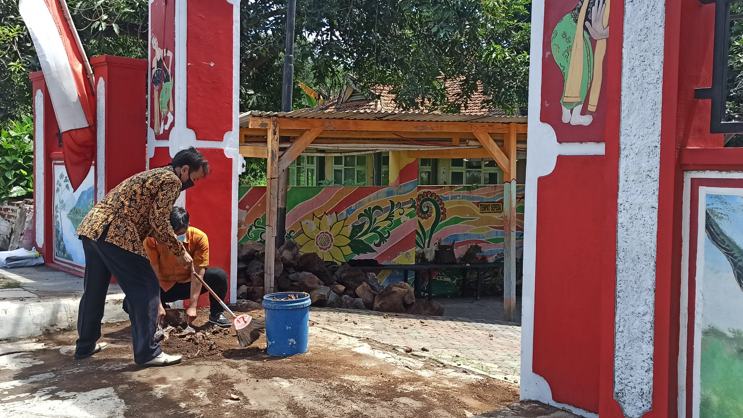 Beberapa petugas membersihkan sisa tumpukan material batu di depan pintu masuk SDN Klatak, Kecamatan Kalipuro, Banyuwangi (foto:Muh Hujaini/Ngopibareng.id)