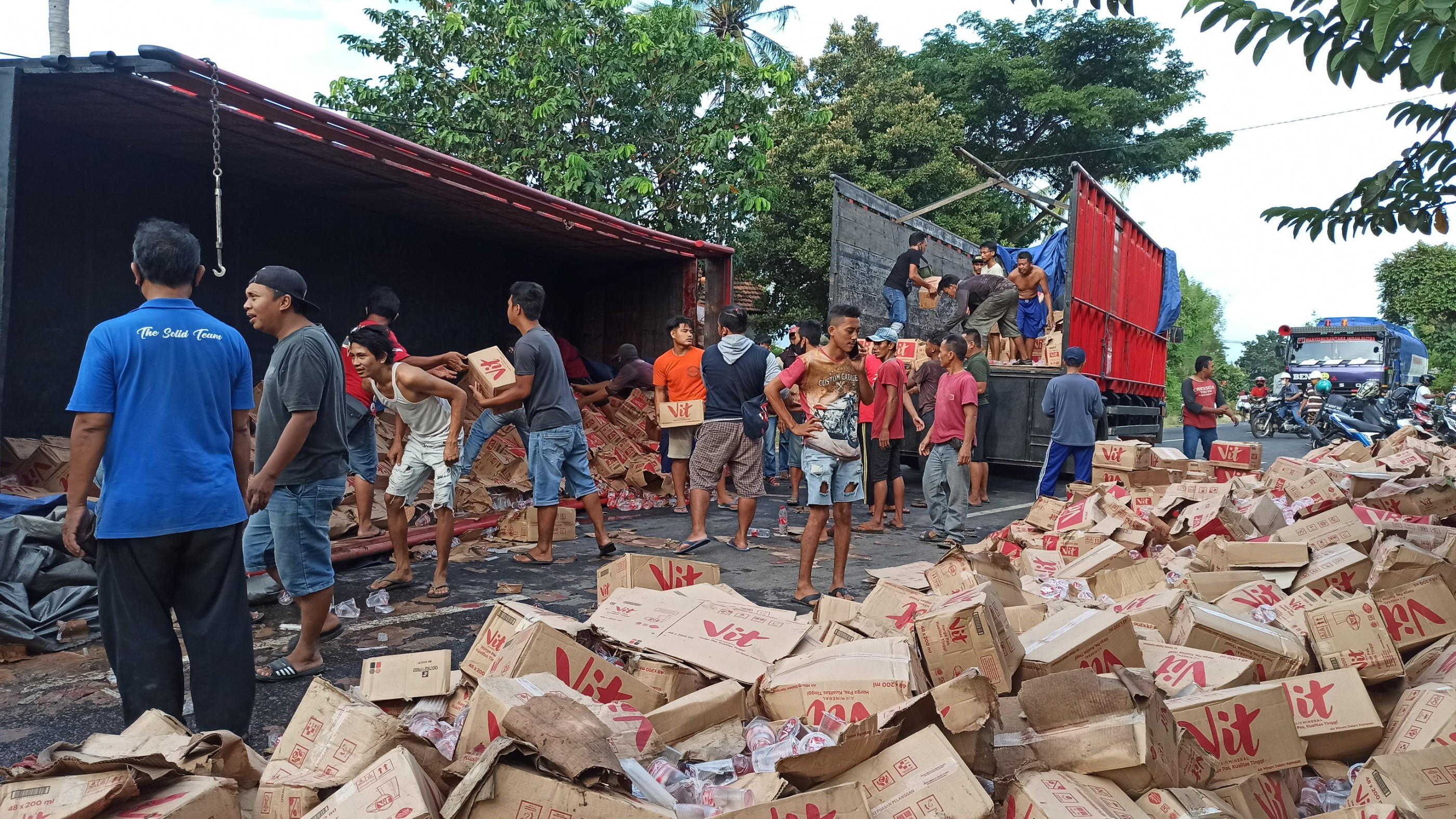 Warga memindahkan air mineral muatan truk yang terguling ke truk yang lain (foto:Muh Hujaini/Ngopibareng.id)