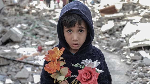 Seorang anak laki-laki memegang bunga di antara puing-puing setelah rumah keluarga Palestina Al Deyri yang dihancurkan oleh serangan udara tentara Israel di Kota Gaza,  pada Senin 17 Mei 2021. (Foto: Ali Jadallah/Anadolu Agency)