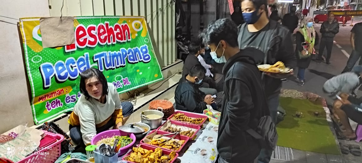 Endah salah satu pedagang lesehan pecel tumpang di Jalan Dhoho yang mengaku sepi jualannya pembeli gegara video viral pecel Jalan Dhoho mahal. Endah sendiri menjual dengan harga normal Rp8 ribu per porsi. Menu daftar harga juga dicantumkan. (Foto: Fnedhy Plesmana/Ngopibareng.id)