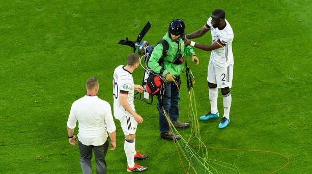 Antonio Rudiger membantu penerjun untuk berdiri sesaat setelah mendarat di lapangan. (Foto: Dailystar)