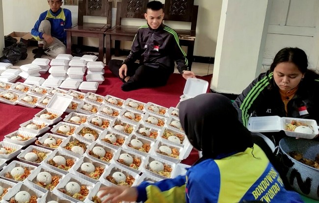 Taekwondoin putra dan putri Bondowoso menata nasi bungkus hasil urunan yang akan dibagikan kepada tukang becak dan pengemis di pinggir jalan Kota Tape. (Foto: Guido Saphan/Ngopibareng.id)