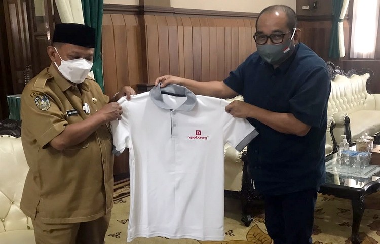 CEO Ngopibareng.id, Arif Afandi menyerahkan suvenir kaos bertuliskan Ngopibareng.id kepada Bupati Situbondo, Karna Suswandi di Pendapo Bupati Situbondo, Jawa Timur. (Foto: Dok. Ngopibareng.id.)