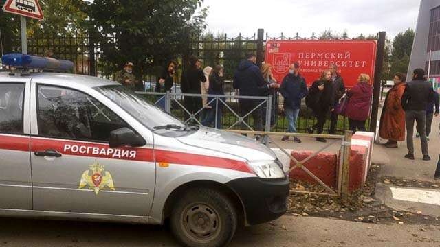 Orang-orang berdiri di belakang pagar Kampus  Universitas Negeri Perm yang dijaga petugas keamanan, di Kota Perm, Rusia, Senin, Senin pagi 20 September 2021 (Foto:/AP/Al Jazeera)