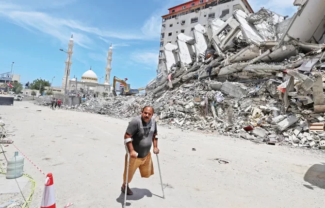 Seorang pria Palestina cacat berjalan melewati puing-puing bangunan yang dihancurkan oleh serangan udara Israel di Kota Gaza pada bulan Mei. Miliaran dibutuhkan untuk membangun kembali kota. (Foto: AFP)