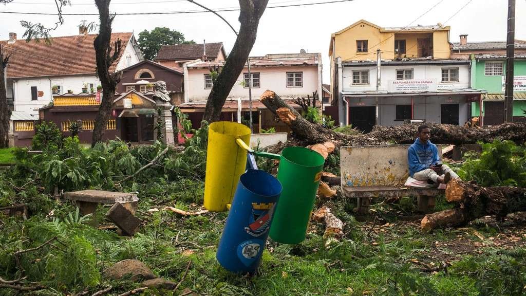 Seorang pria duduk di bangku di antara pohon yang tumbang di taman umum di pusat Antsirabe setelah topan Batsirai, Madagaskar Minggu 6 Februari 2022. (Foto: AFP)