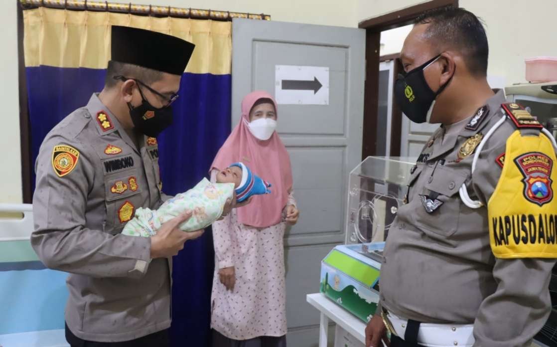 Kapolres Bondowoso AKBP Wimboko menggendong bayi perempuan mungil didampingi Kasat Lantas AKP Didik Sugiarto di Puskesmas Curahdami. (Foto: Guido Saphan/Ngopibareng.id)