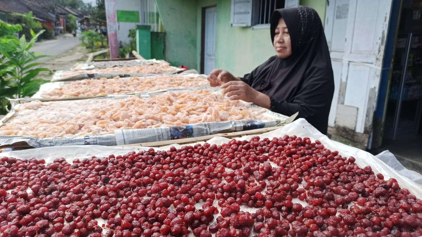 Suswati sedang menjemur manisan buah pala dan cermai di halaman rumahnya. (Foto: Muh Hujaini/Ngopibareng.id)