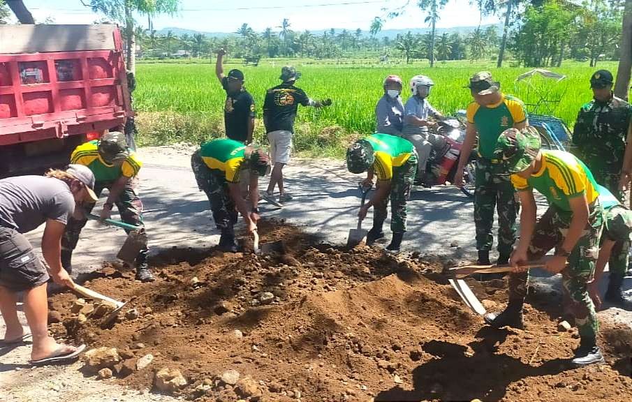 Warga dan anggota TNI di Bondowoso gotong royong menambal jalan rusak yang dua tahun tak kunjung diperbaiki Pemkab Bondowoso.(foto:guido saphan/ngopibareng.id)